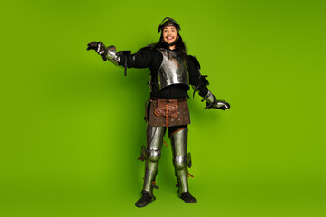 Fototapeta premium Medieval knight in full armor posing against vibrant green background with a cheerful and humorous demeanor