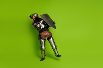 Young knight in full medieval armor posing with a shield on a vibrant green background