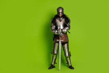 Fototapeta premium Medieval knight in shining armor holding a sword against a vibrant green backdrop, vividly illustrating historical themes and modern.