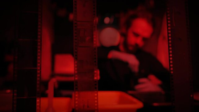 Developing photos in a photography studio. Old school photo film negatives hanging to dry. Darkroom with red light. Man working