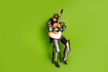 Armored Medieval Knight Playing Acoustic Guitar Against Vibrant Green Background Depicting Modern Twist on Historical Theme