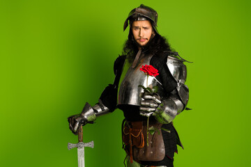 Naklejka premium Young medieval knight in steel armor holding a rose against green background, showcasing a blend of history, romance, and humor.