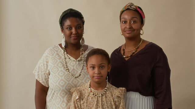 Zoom out portrait shot of young African American girl standing in front of two women, all dressed in patterned clothing and wearing jewelry