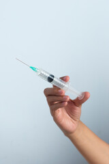 Asian woman's hand holding an injection on a white background. The hand holds a syringe.