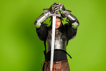 Fototapeta premium Knight in shining armor posing heroically in a medieval style costume with a sword against a vibrant green backdrop