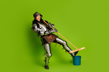 Funny medieval knight posing with a mop on a vibrant green background
