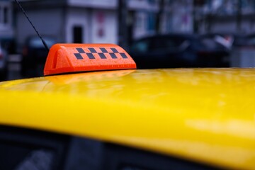 Bright yellow taxi with an orange light on top parked on a bustling city street during a rainy day