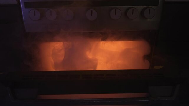 Close-up of a hand opening the oven door as thick smoke billows out, creating a fire-hazardous situation in the kitchen.