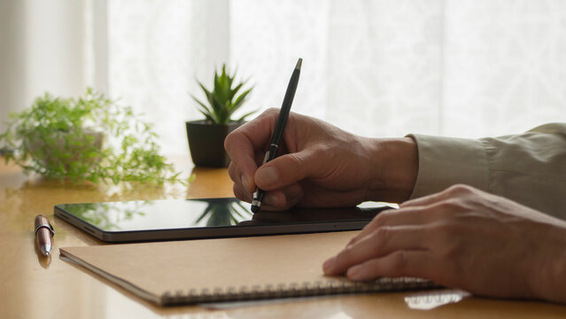 a man's hand writing on a tablet on the table