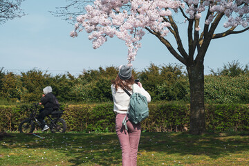 Woman Taking Photo of Blossoms as Cyclist Passes in Westerpark, Amsterdam