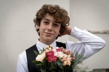 A photo of a 15-year-old boy with curly hair and a coquette pose. He is holding a bouquet of flowers.