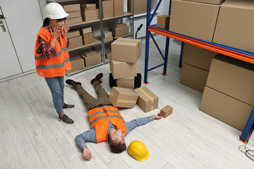 Accident at work. Worried woman and her unconscious colleague in warehouse