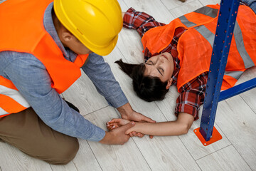 Accident at work. Man checking pulse of his unconscious colleague in warehouse