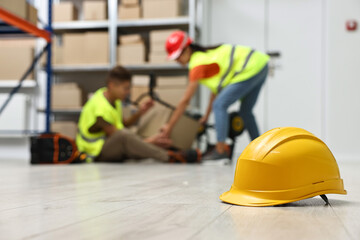 Accident at work. Hardhat on floor and woman helping her injured colleague in warehouse, selective...
