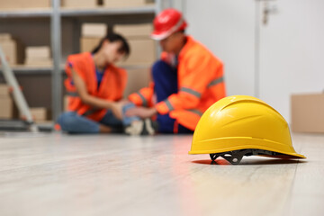 Accident at work. Hardhat on floor and man helping his injured colleague in warehouse, selective...