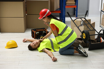 Accident at work. Woman checking pulse of her unconscious colleague in warehouse