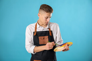 Man with palette and paintbrush on light blue background