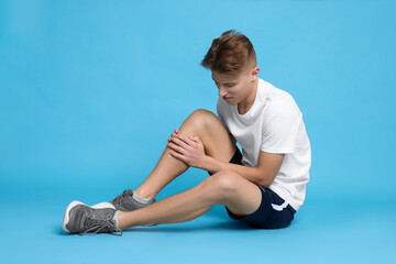 Young man suffering from pain in knee on light blue background