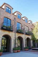 Contemporary brick townhouses featuring stylish balconies are nestled in a sunny neighborhood, surrounded by vibrant greenery and charming warm stone details