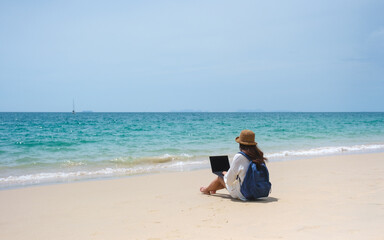 A female traveler using and working on laptop computer while sitting on the beach