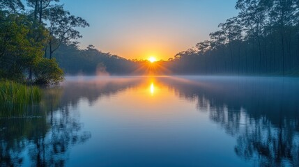 Sunrise over tranquil lake, misty morning, trees reflected in calm water.