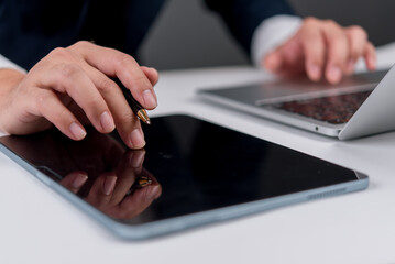 Businessman using tablet and pen for digital signature, with laptop on desk, representing paperless...