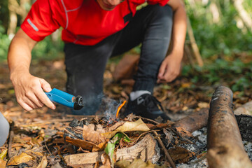 Close-up of lighting fire with lighter on dry leaves during forest camping