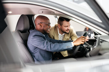 Fototapeta premium A car dealer in a modern car dealership advises an African-American customer on buying or leasing a new car. The concept of an expensive purchase or lease of a modern car.
