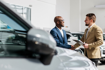 An auto dealer closes a deal or a successful consultation with a handshake with an African-American...