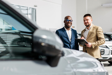 A car dealer in a modern car dealership advises an African-American customer on buying or leasing a...