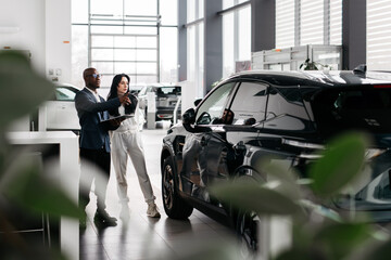 African-American dealer counseling a customer on buying a modern car at a car dealership. Concept...