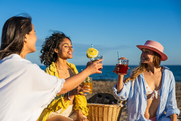 Happy multiethnic women toasting cocktails at beach party