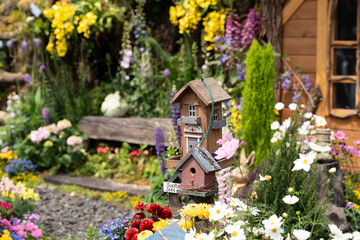 A whimsical birdhouse stands among colorful blooms and garden paths