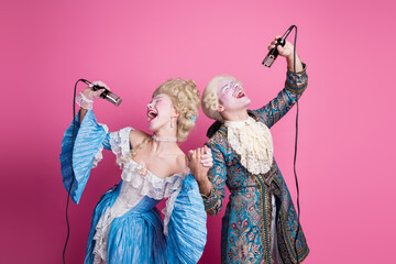 Elegant couple sings joyfully in vintage baroque costumes against pink background at themed party