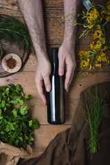 Hands hold a dark wine bottle on a rustic wooden table, surrounded by pumpkin seeds, spices,...