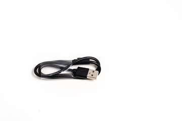 A small, coiled black cable with a USB connector lies on a clean white surface. Soft shadows add depth, emphasizing the simplicity and isolation of the object