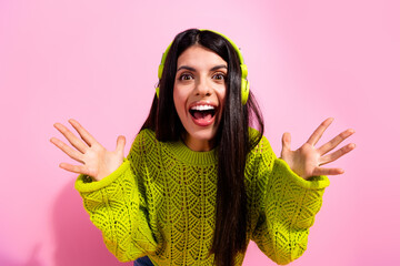 Excited young woman in casual bright outfit enjoying music with headphones, celebrating a happy moment against a colorful pink background