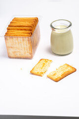  Crispy crackers in a clear container and a small jar of milk on a clean white surface. Simple food still life