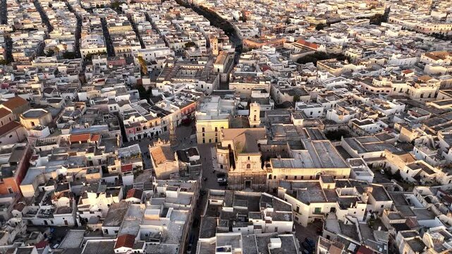 Aerial drone view of Nardo, a historic town in southern Italy, bathed in golden sunset light. The old towns dense architecture, whitewashed buildings, and narrow streets highlight its rich cultural