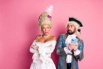 Playful couple in modernized royal costumes posing against a pink background