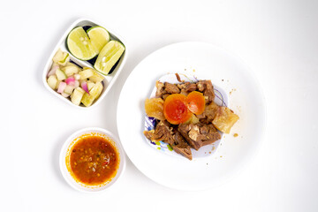Overhead view of Soto Madura ingredients: beef, tomatoes, and potatoes in a white bowl, with lime, pickles, and sambal on a clean white surface.
