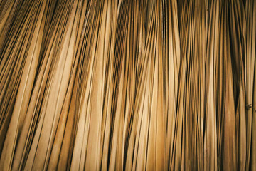 a thatch roof interior. dried grass or vertical strands of bamboo. organic straw abstract honey gold yellow curtain fringe background. creative pattern with contrasts of brown and natural tones.