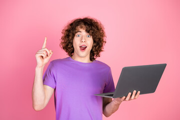 Surprised young man with curly hair holding a laptop and gesturing an idea on a pink background
