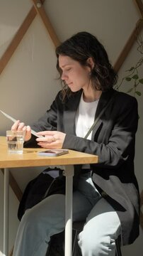 Сharming curly brunette woman sitting in cozy cafe, reading menu and choosing breakfast, brunch, or dessert with coffee. elegant female customer enjoying relaxing atmosphere in a modern coffee shop