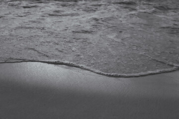 ocean wave edge receding background. wave's edge is clearly defined by a line of foam, and the wet sand reflects light. blank space for copy. tropical vacation or calming design element