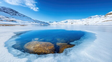 Obraz premium A stunning scene of a snow-covered landscape featuring a stunningly clear pool of water amid striking rocky formations and icy surroundings reflecting the blue sky.