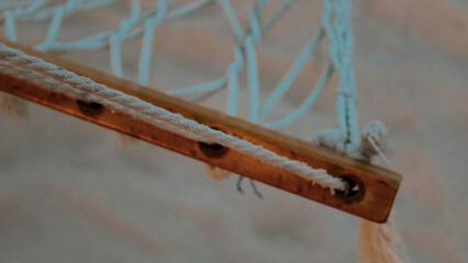 macro close-up of a handwoven hammock wooden rung with threaded rope and netting tropical vacation design element and defocused sand background.