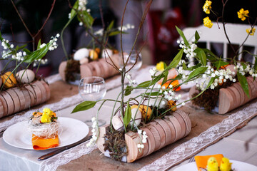 Easter table setting in yellow colors with floral arrangements of yellow flowers, eggs and lilies of the valley