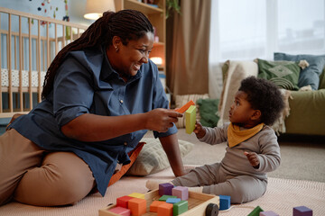 Smiling Black woman looking at little daughter with love and affection spending time with baby girl...