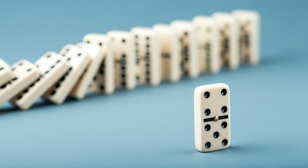 A single domino piece stands upright in front of a falling line of dominoes